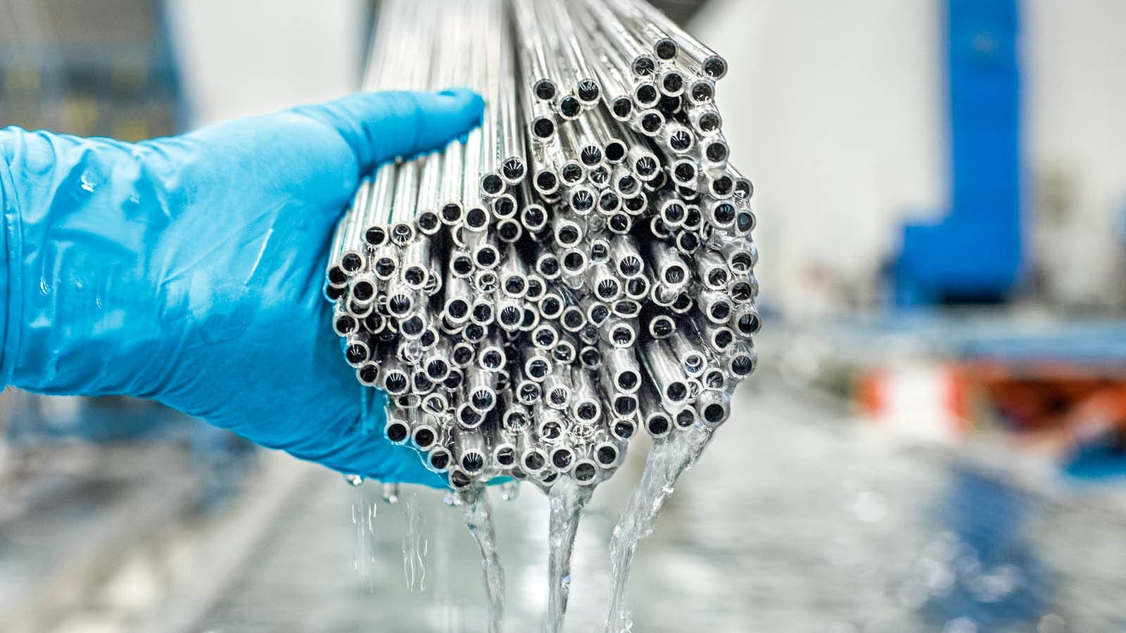 A hand wearing blue gloves holds a bundle of tubes that has just been cleaned