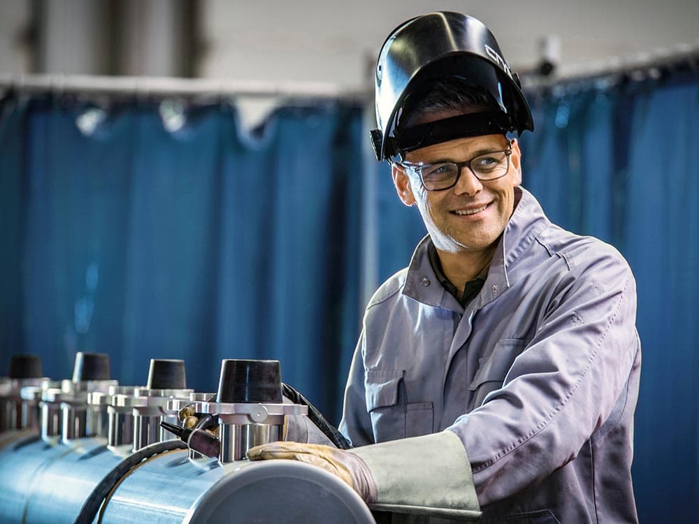A welder is standing next to a manifold and wearing a welding  helmet