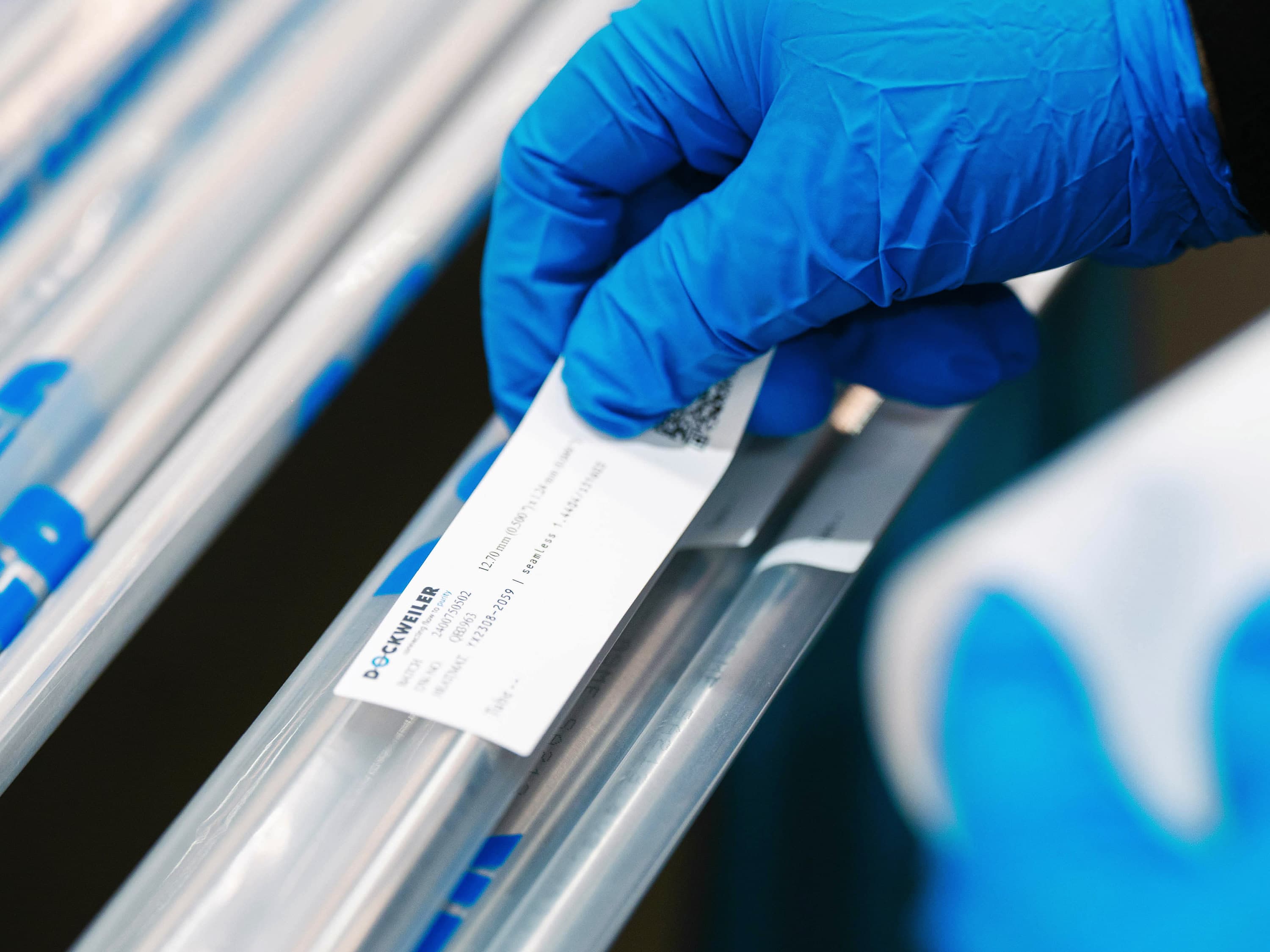 Hand in blue glove sticking label on Dockweiler tube; tube is packed in Dockweiler tubular film
