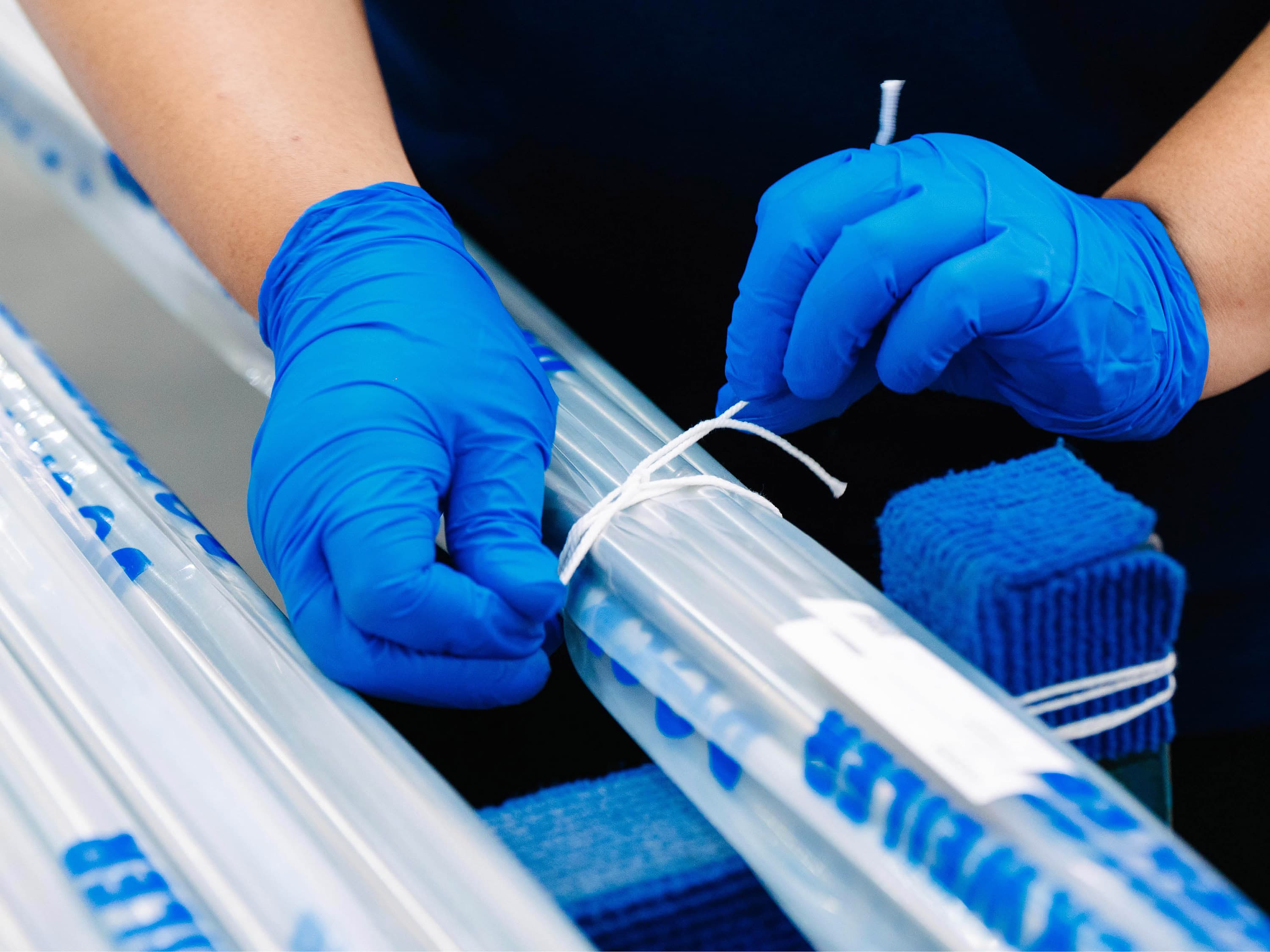 A hand wearing blue gloves packs tubes that are covered in a Dockweiler tubular film.