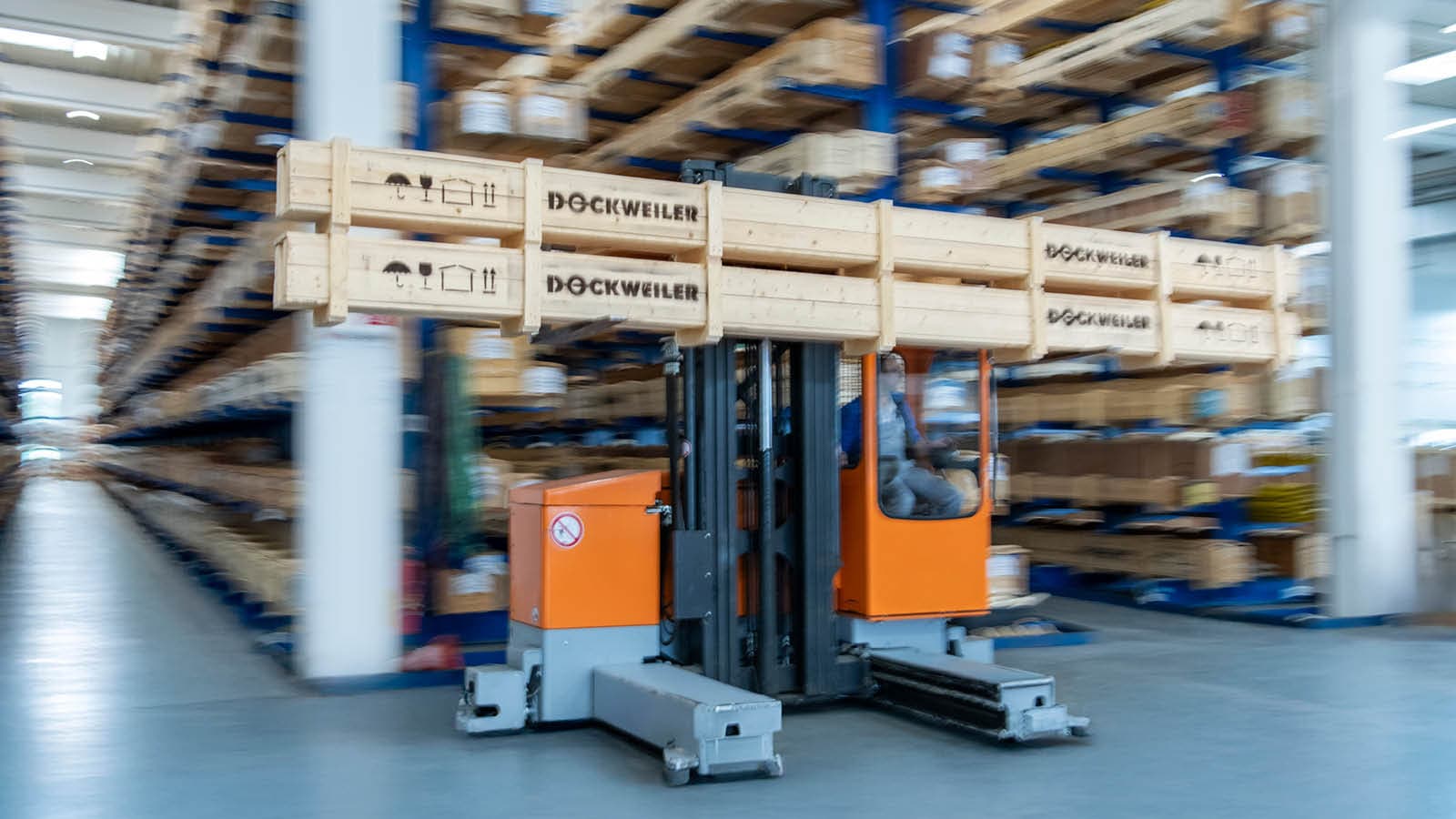 Forklift truck with two wooden boxes on the fork in front of a high rack in a large warehouse